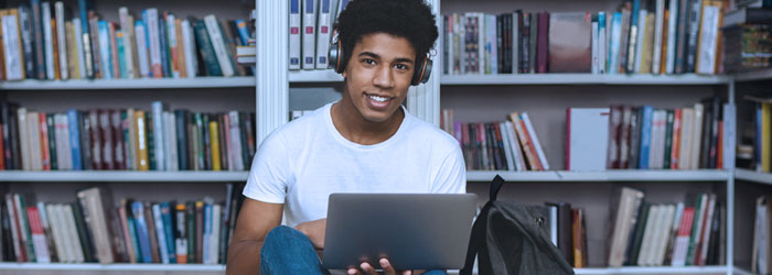 Mundo VUCA: Jovem sentado em biblioteca com fone de ouvido e computador no colo.